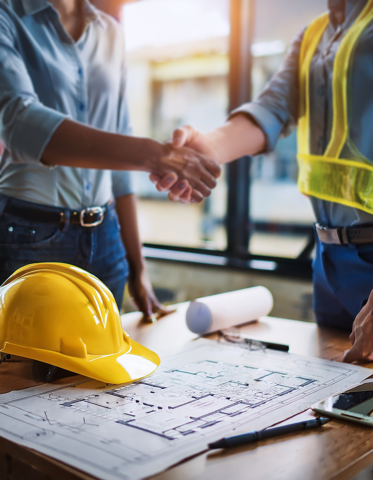 Contractor and client shaking hands over construction plans and safety equipment