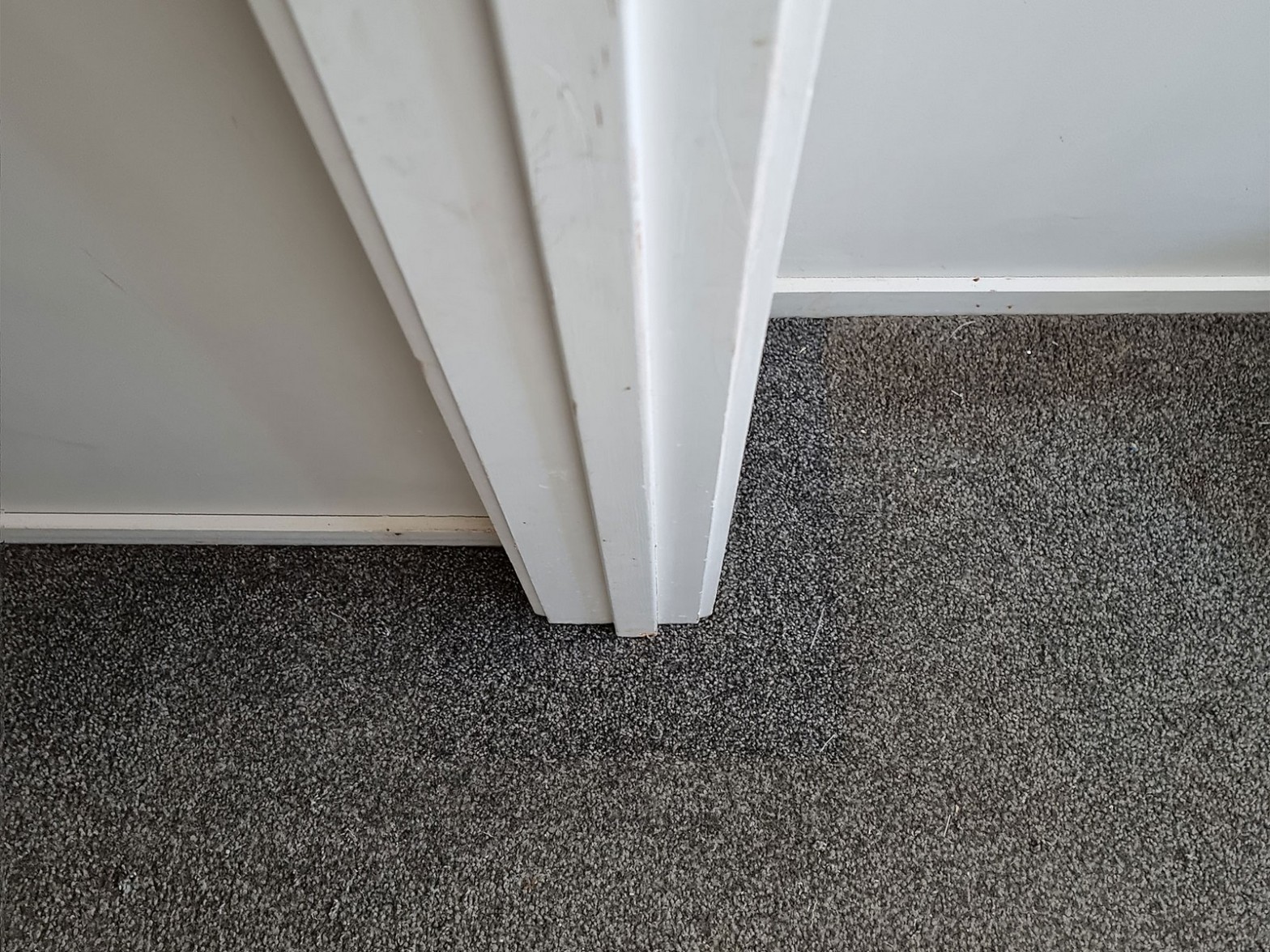 Grey carpet fitted neatly at white door frame corner