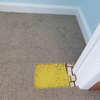 Carpet with yellow underlay exposed at door frame before patching