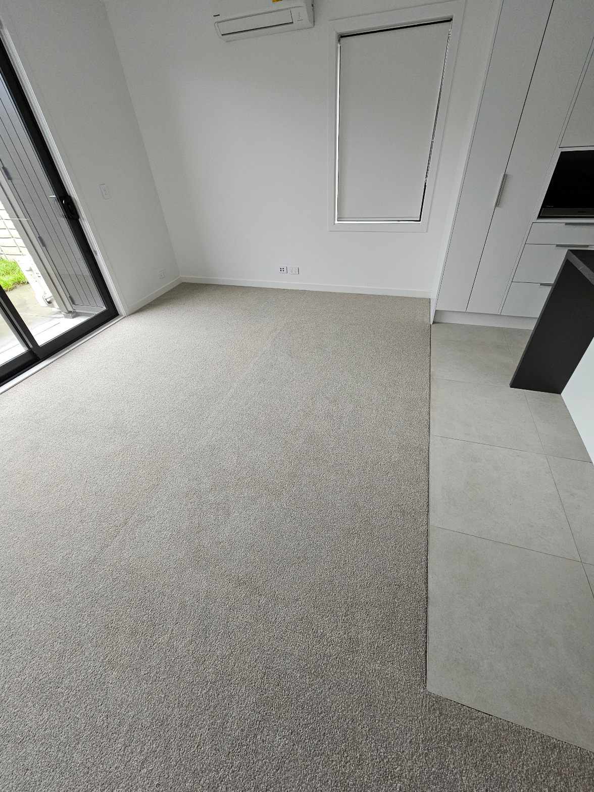 Clean light grey carpet laid in open plan room next to tiled kitchen area