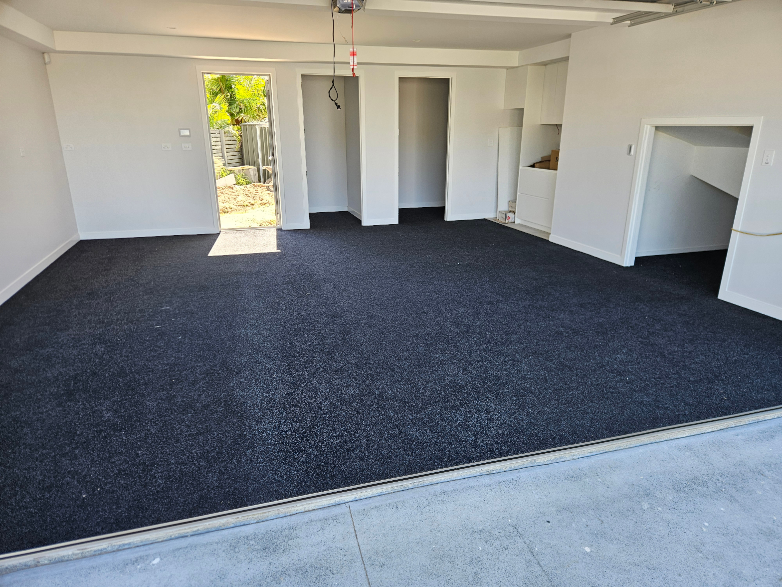Dark navy garage carpet fully laid with clean white walls and open garage door