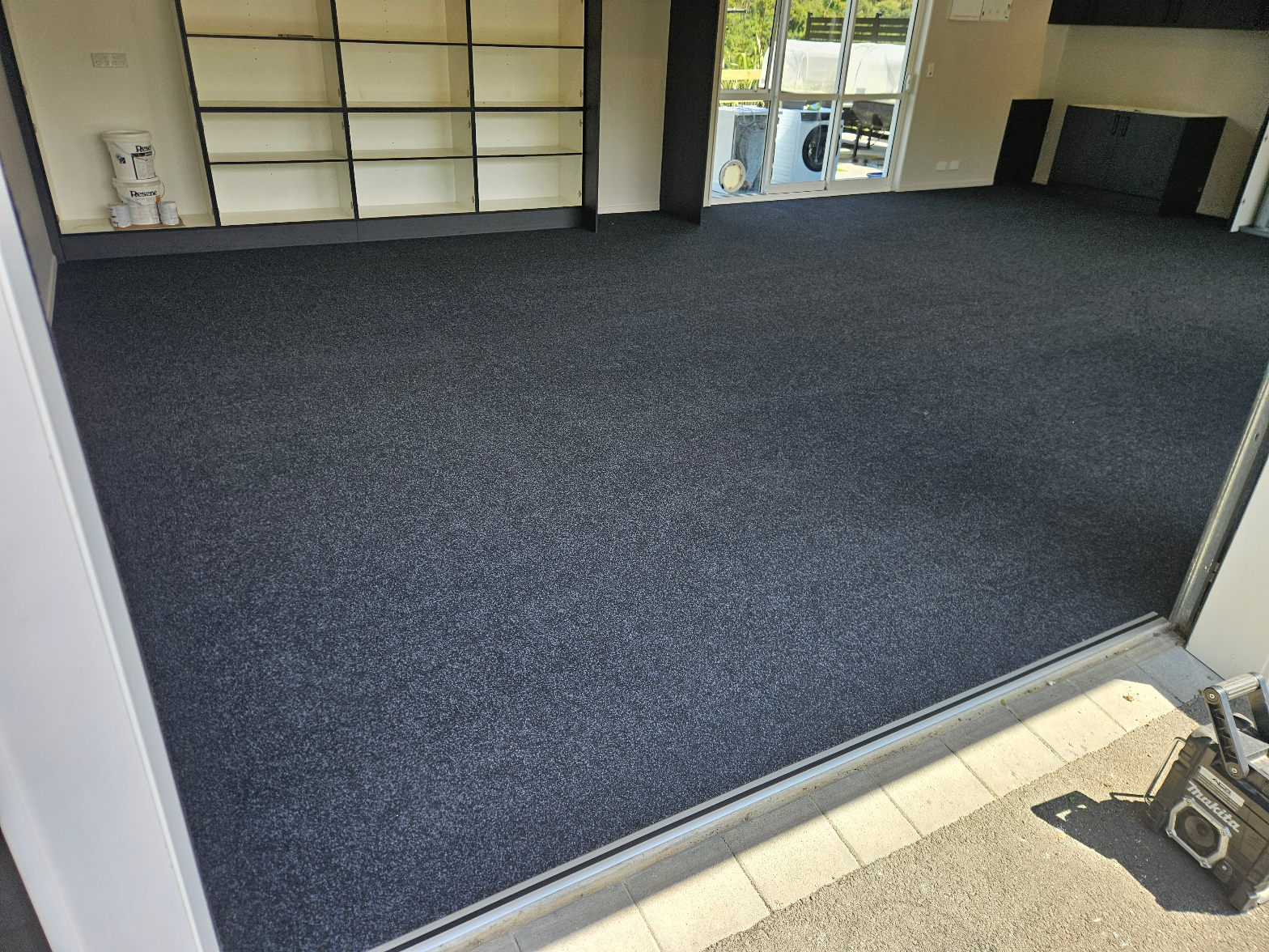 Dark charcoal garage carpet fully installed across a large open double garage with shelving and sliding door