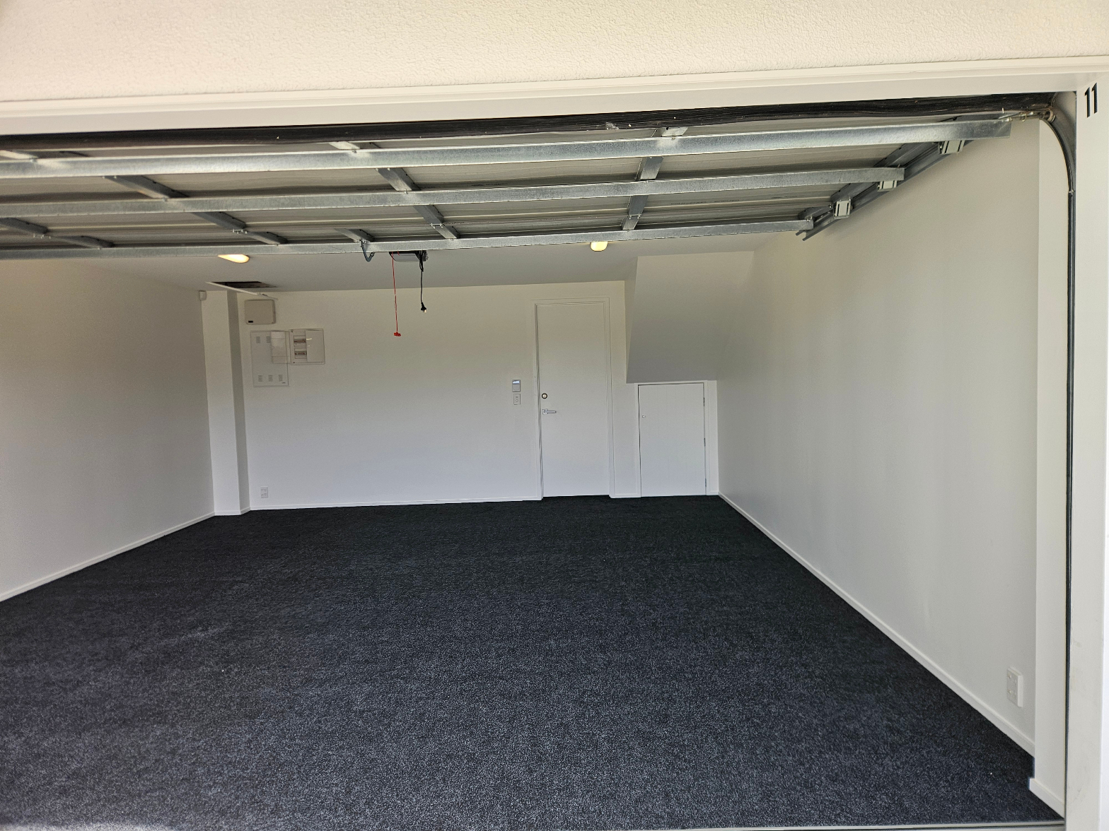 Clean dark charcoal carpet fitted in a bright white double garage with roller door open and internal access door