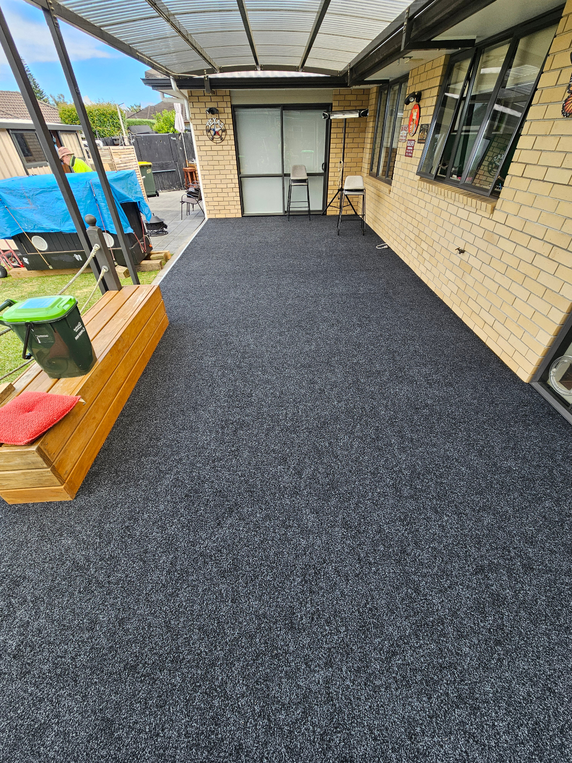 Dark charcoal carpet laid across a large covered outdoor entertainment area next to brick house