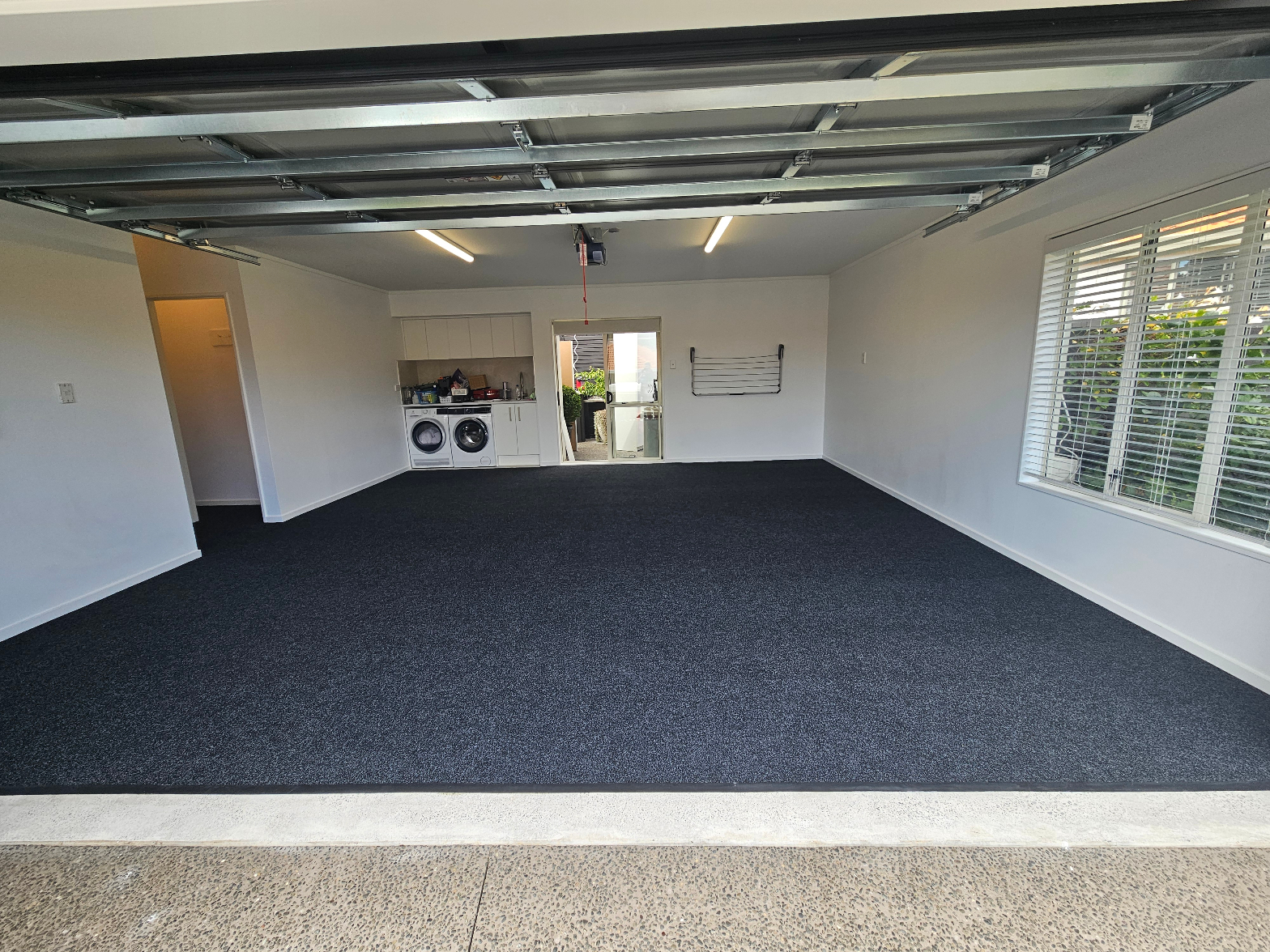 Dark charcoal carpet fully installed across a double garage conversion with laundry area and open roller door