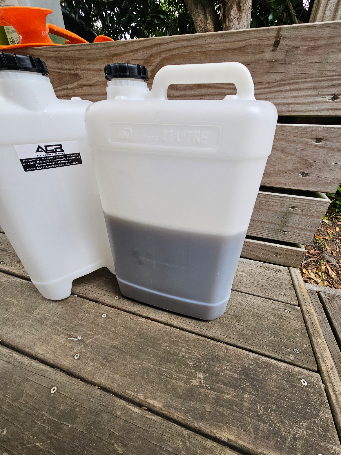 ACR-branded cleaning solution jugs showing dirty extracted water after carpet cleaning