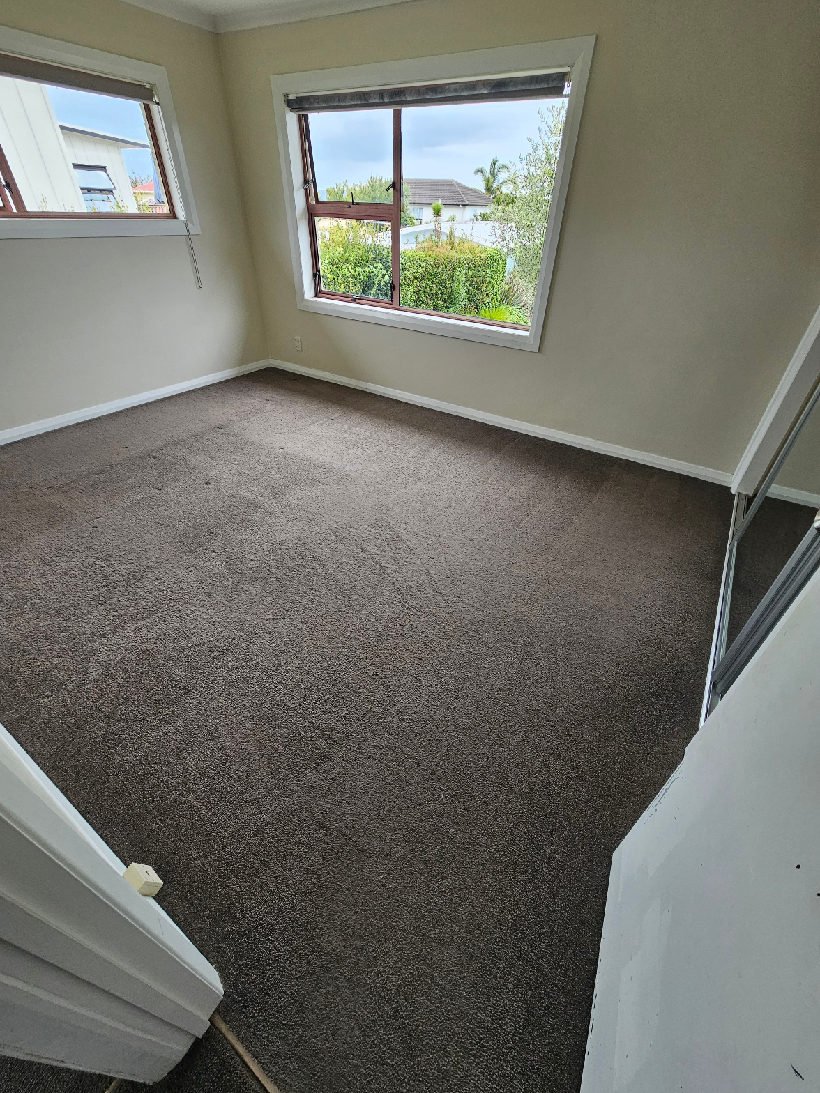 Clean dark brown carpet in an empty bedroom with large windows overlooking a garden