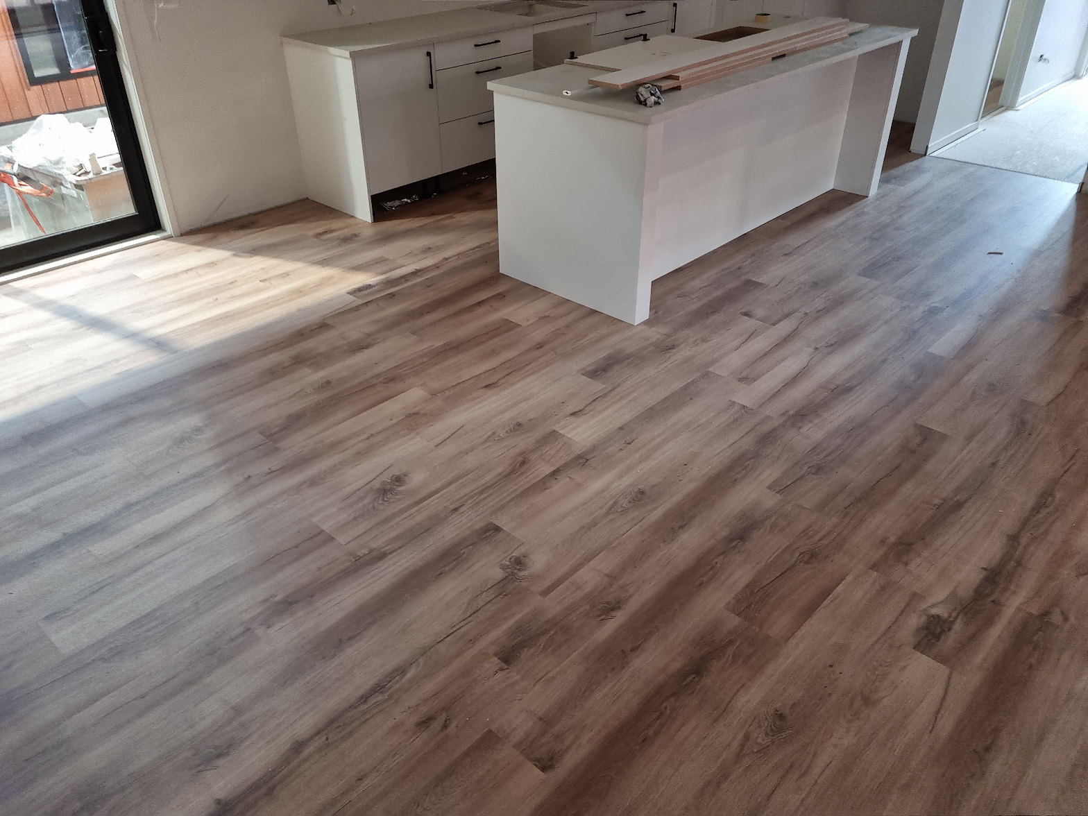 Freshly installed grey-brown laminate flooring in a new build open-plan kitchen