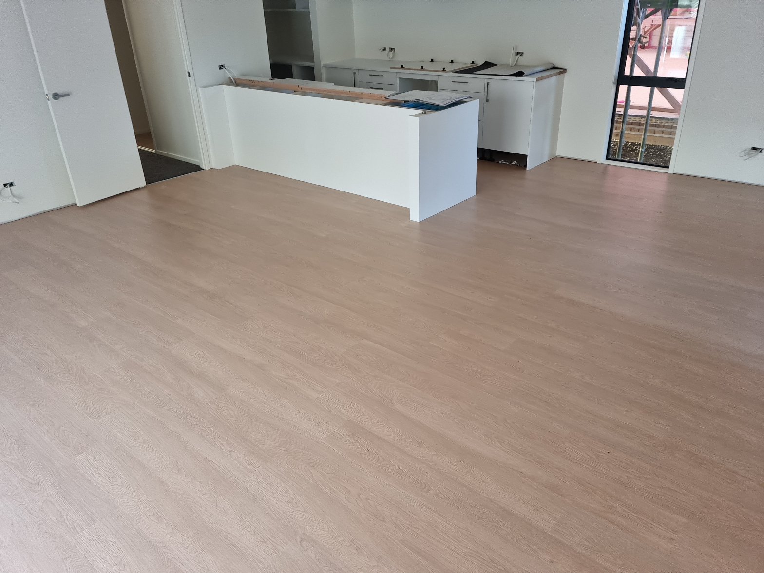 Light oak laminate flooring freshly installed in an open-plan new build with white kitchen cabinetry