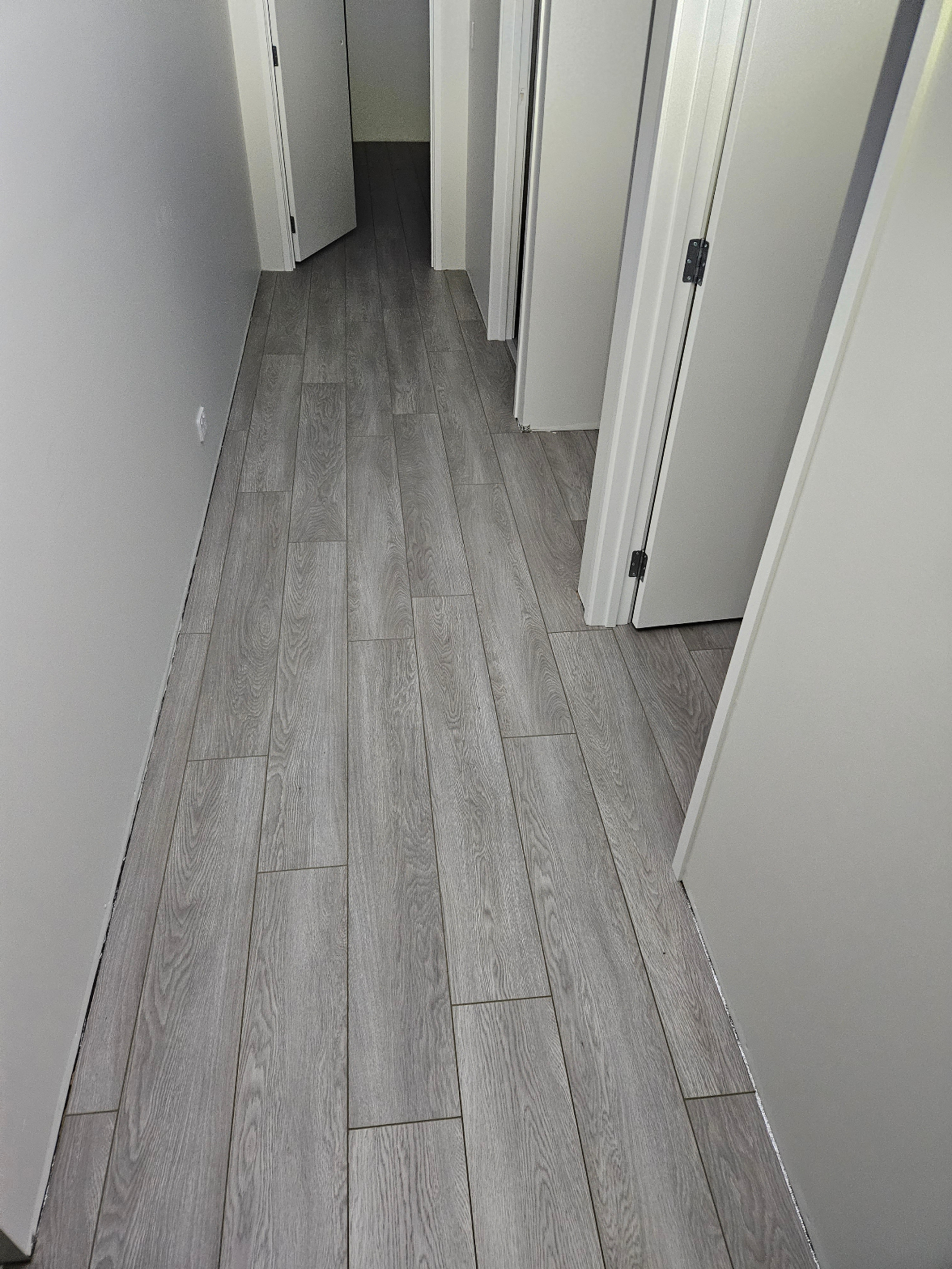 Grey laminate flooring freshly installed in a hallway with white door frames