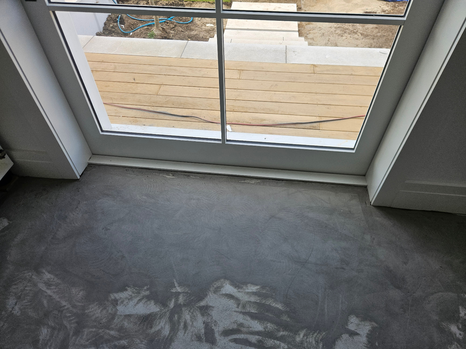 Dried self-levelling compound on a concrete subfloor viewed from a sliding door looking out to a timber deck during new build floor preparation